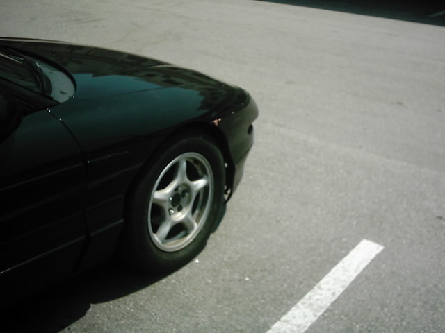 Front corner of a black sports coupe with five-spoke alloy wheel in a parking lot