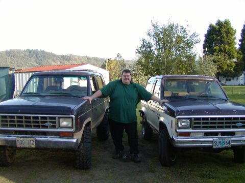 1987 Ford Bronco II - A man poses between two Ford Bronco II SUVs, one dark blue and the other a two-tone model.
