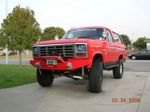 1985 Ford Bronco - This red Ford Bronco features a prominent winch and aftermarket bumper, suggesting off-road modifications.