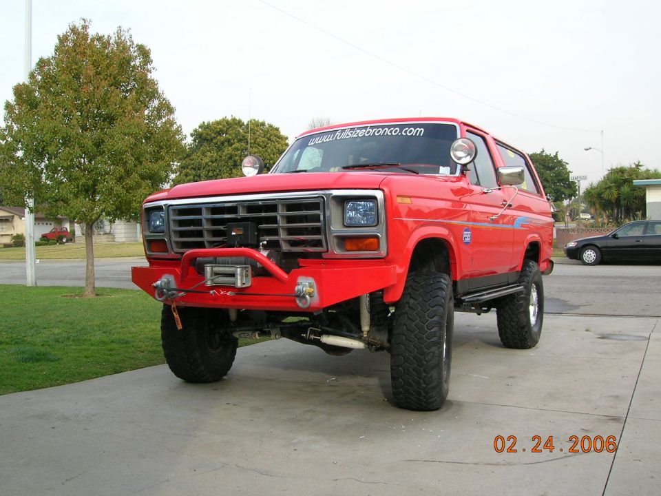 Red Ford Bronco with custom front bumper, winch, and off-road tires parked on a driveway