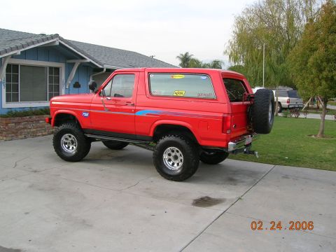 1985 Ford Bronco - A red Ford Bronco is parked in front of a blue house, with another vehicle visible in the background.