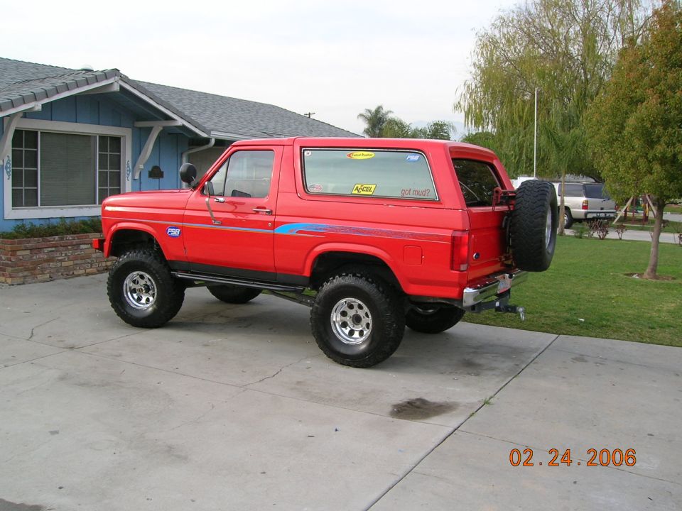 Red lifted Ford Bronco with off-road tires parked on a driveway, rear-mounted spare tire visible