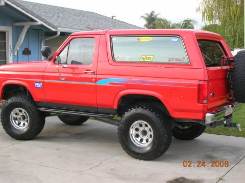1985 Ford Bronco - This red 1985 Ford Bronco features a lifted suspension, off-road tires, and a spare tire mounted on the rear tailgate.