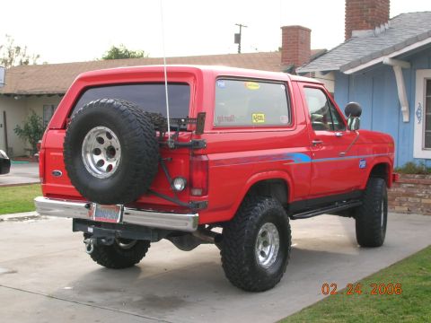 1985 Ford Bronco - This red 1985 Ford Bronco is parked in a residential driveway with a spare tire on the back.