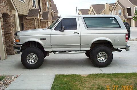 1996 Ford Bronco - A silver 1996 Ford Bronco SUV is shown from the side, parked in front of a residential building.