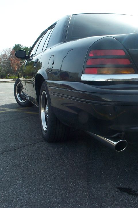 1999 Ford Crown Victoria - Low-angle rear three-quarter shot of a black Ford Crown Victoria sedan showing the driver's side rear quarter, taillight, and a large chrom…