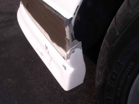 1996 Ford Probe - Close-up of a damaged white car fender with visible body filler next to a tire.