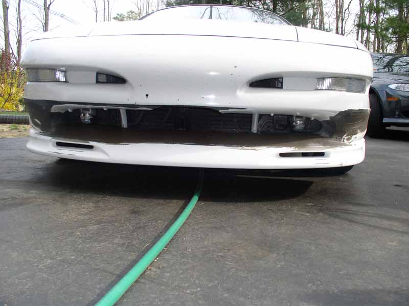 1996 Ford Probe GT front bumper with damage and a green hose underneath