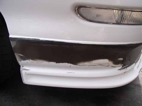 1996 Ford Probe - The front bumper of a white car shows significant paint damage and wear.