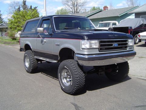 1989 Ford Bronco - A modified Ford Bronco with a lifted suspension and large off-road tires is parked on a residential street.