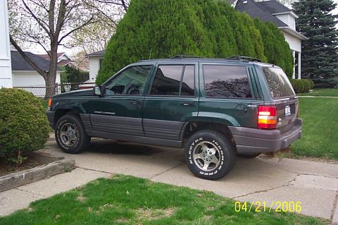 1978 Ford Bronco - This Jeep Grand Cherokee is parked on a concrete driveway in front of a house and trees.