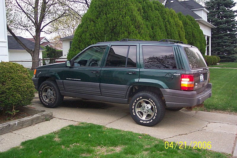 Green Jeep Grand Cherokee parked on a driveway, side view. Tires have white lettering