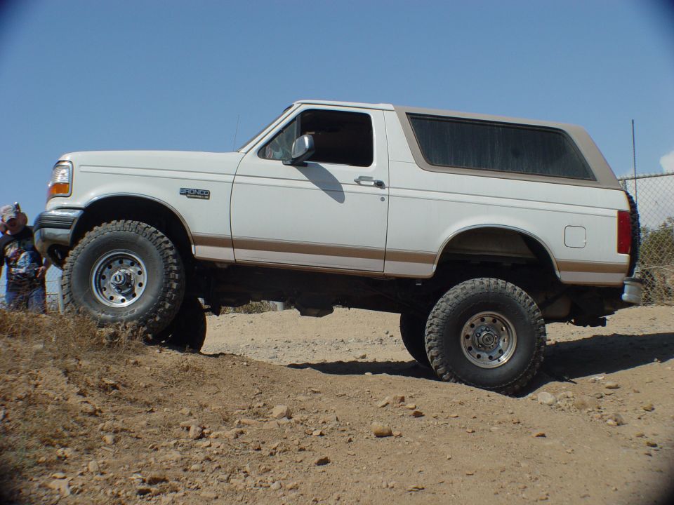 White 1996 Ford Bronco with tan top driving on a dirt hill