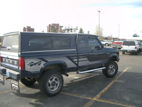 1992 Ford Ranger - A Ford Ranger pickup truck with a camper shell is parked in a lot, showing its 4x4 graphics.