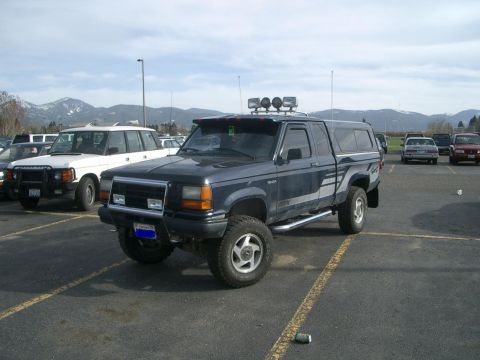 1992 Ford Ranger - A dark blue 1992 Ford Ranger pickup truck is parked in a lot with other vehicles and mountains in the background.