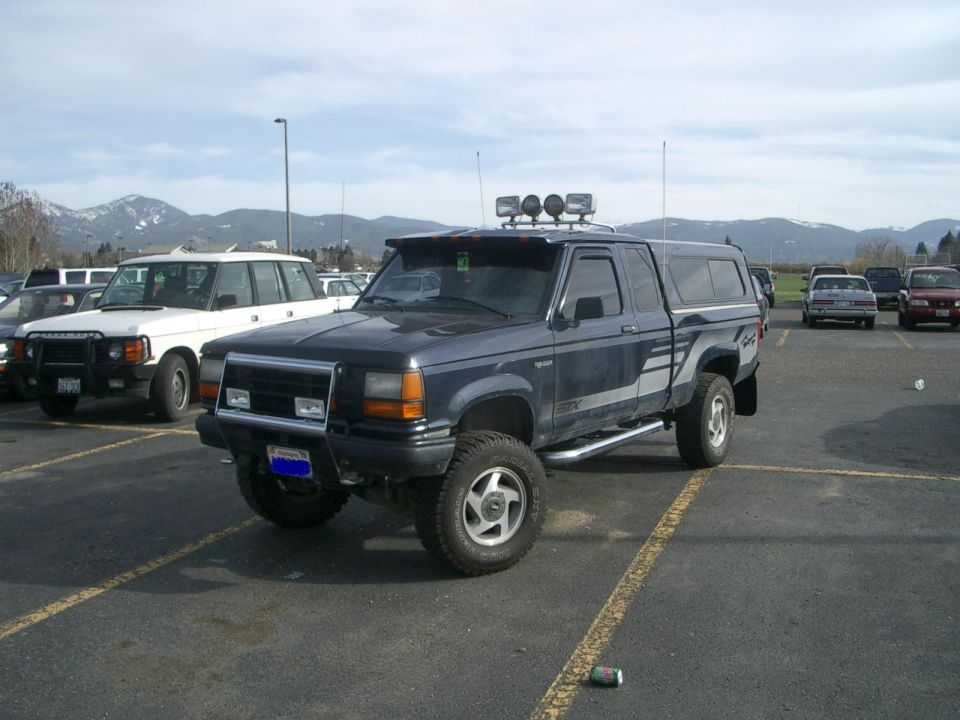 Dark blue 1992 Ford Ranger pickup truck with a camper shell, aftermarket wheels, and a light bar on the roof