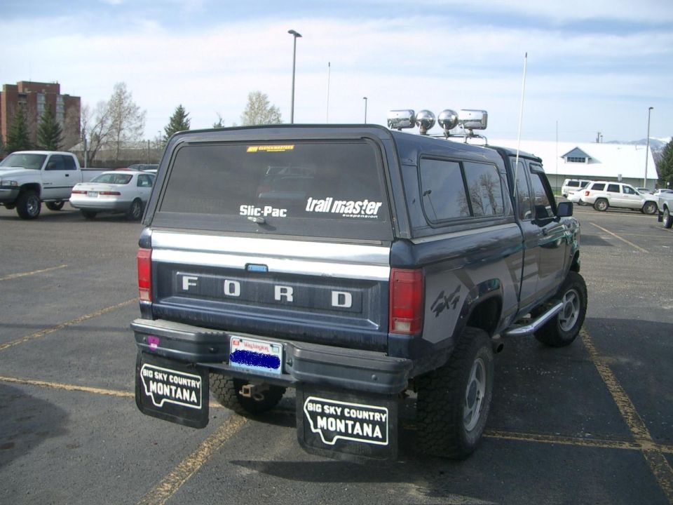Rear view of a dark blue Ford pickup with a camper shell and mud flaps that say 'Big Sky Country Montana'