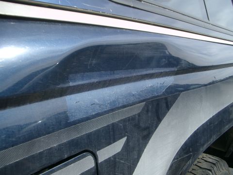 1992 Ford Ranger - A dented blue truck fender shows signs of repair with tape and has a graphic stripe.