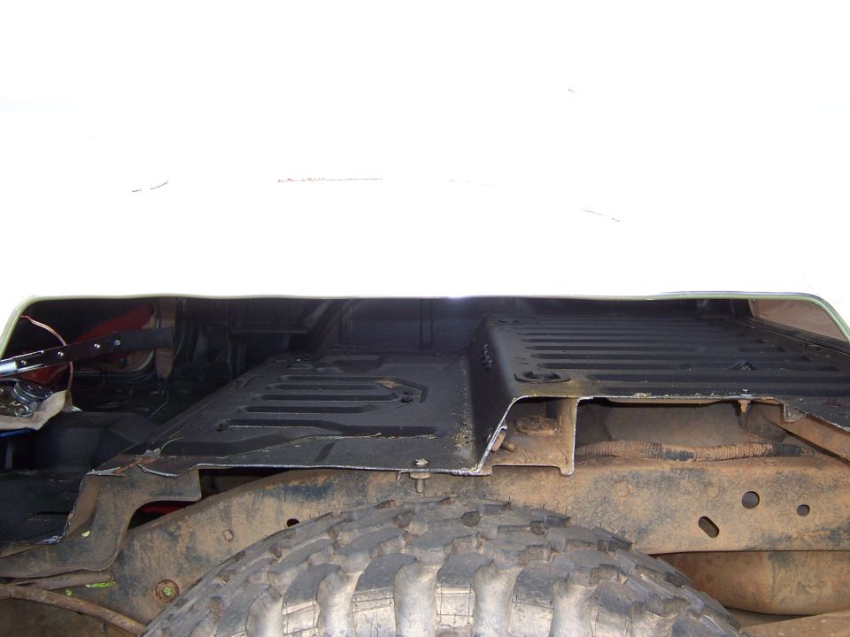 view of the floor pan and frame of a vehicle, showing rust and a large tire
