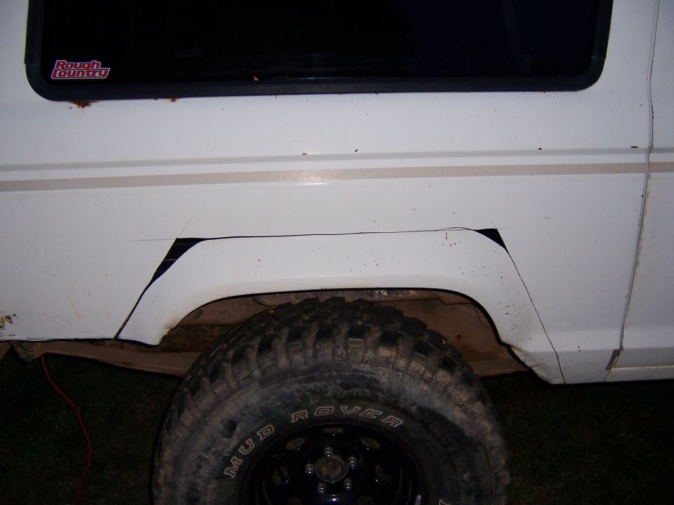 White SUV's rear wheel well with a 'Rough Country' sticker on the window. The fender flares have been cut