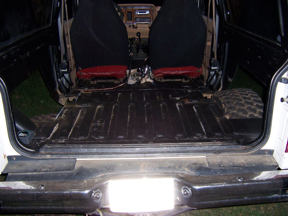 Interior of a white SUV with black seats and a bare cargo floor, showing a spare tire in the rear