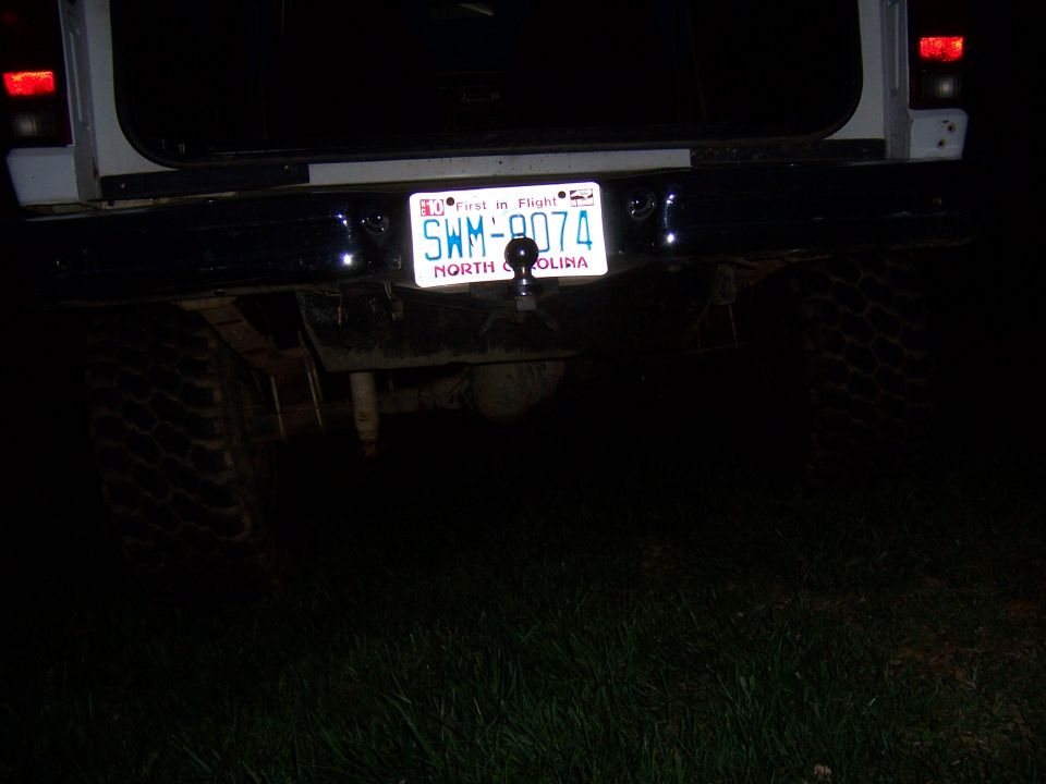 Vehicle rear bumper with North Carolina license plate SWM-9074, tow hitch, and tire visible in darkness