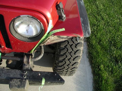 1998 Jeep TJ - The front fender of a red Jeep Wrangler shows damage, with green tape used for temporary repair.
