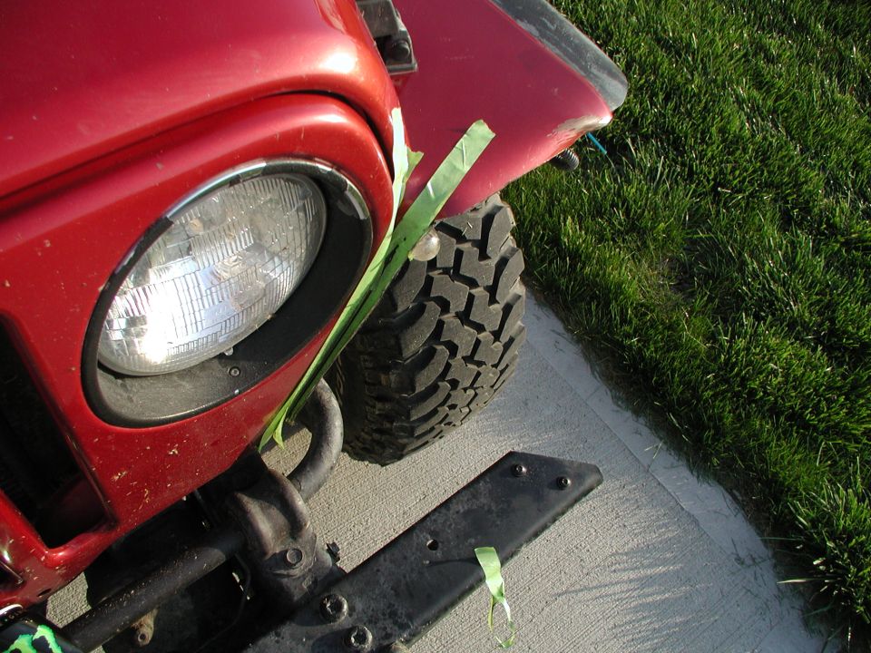 Overhead close-up of red Jeep Wrangler front corner with headlight, flare and mud tire