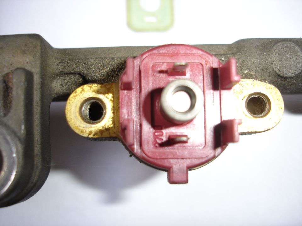 Close-up of an aluminum fuel rail with red plastic regulator mount and brass bolt flanges