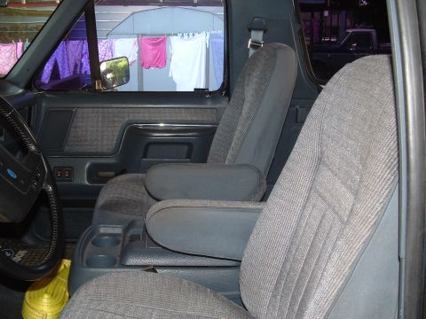 1989 Ford Bronco - The interior of a vehicle is shown, cloth seats and a center console with cup holders.