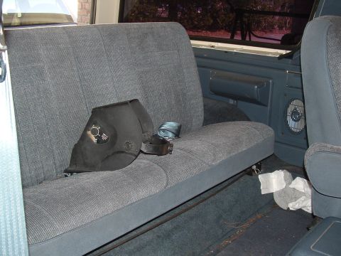 1989 Ford Bronco - A welding mask rests on the rear seat of a vehicle, next to a seatbelt and some crumpled paper.