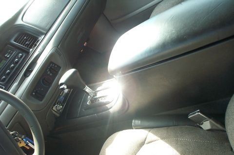 1999 Ford Crown Victoria - Interior view of a gray sedan cabin showing a floor-mounted automatic shifter with chrome gate and a long black padded center console armre…