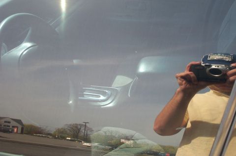 1999 Ford Crown Victoria - Interior detail shot taken through a closed side window, showing the steering wheel and part of the gray dashboard; heavy glare and the pho…