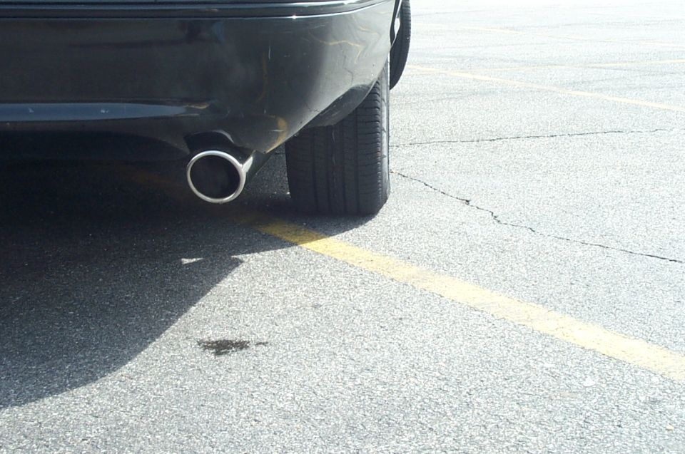 Chrome exhaust tip and rear tire of a dark sedan on cracked asphalt