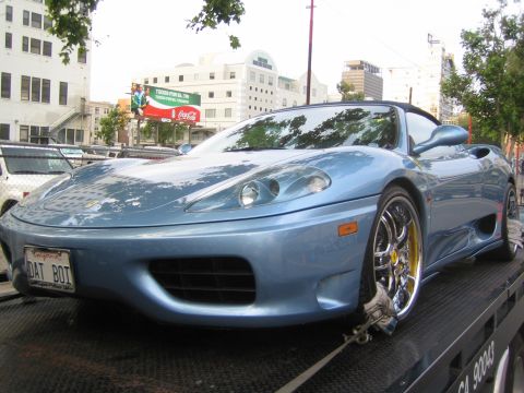 1990 Ford Bronco - Front three-quarter view of a light blue Ferrari convertible on a flatbed, showing a 'DAT BOI' plate and a Coca-Cola billboard behind.