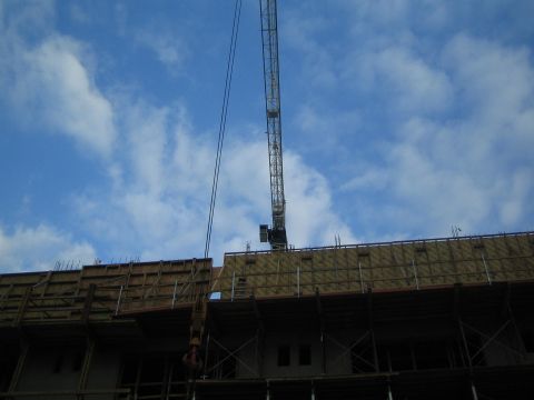 1990 Ford Bronco - tall tower crane rises against a partly cloudy blue sky above the wood-framed upper floor of a building under construction.