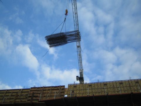 1990 Ford Bronco - crane hoists a large bundle of rebar high against a blue, cloud-streaked sky above a yellow-formed construction deck.