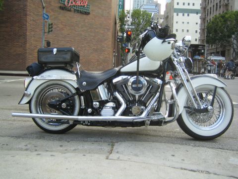 1990 Ford Bronco - black-and-white Harley-Davidson softail cruiser with whitewall tires, hard saddlebags, and chrome engine sits parked at a downtown curb.