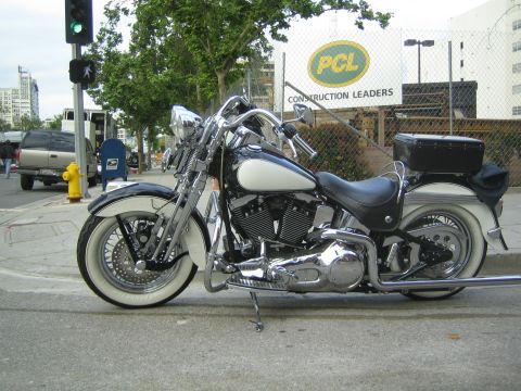1990 Ford Bronco - Side view of a black-and-white cruiser motorcycle with saddlebags and whitewall tires parked at a street corner near a PCL Construction sig…