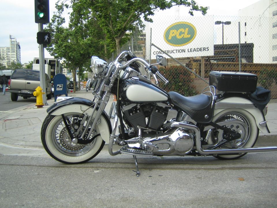 Black and white cruiser motorcycle with saddlebags parked at a corner by a PCL sign