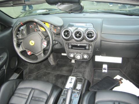 1990 Ford Bronco - Interior of a black Ferrari convertible showing the steering wheel with prancing-horse badge, three round center vents, and dark trim conso…