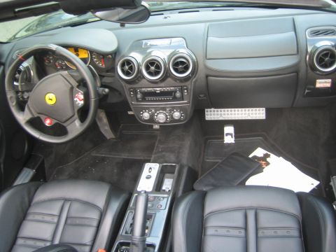 1990 Ford Bronco - Cockpit of a black Ferrari convertible with leather bucket seats, a metal gated shifter, drilled pedals, and three round dashboard vents.