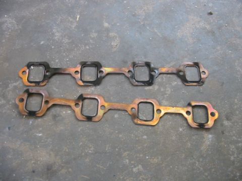 1985 Ford LTD Crown Victoria - Two exhaust manifold gaskets are shown laid out on a gray, textured surface.