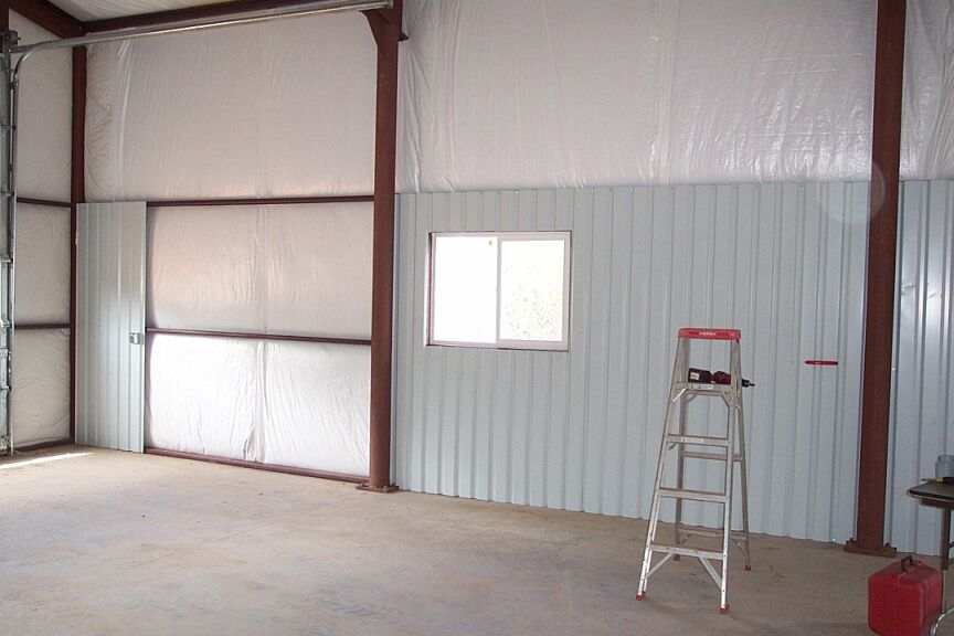 Empty steel shop interior with green metal wainscot, ladder, drill and gas can on concrete floor