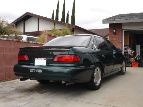 1993 Ford Taurus - A dark green 1993 Ford Taurus SHO sedan is parked in a driveway, viewed from the rear.