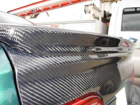 1993 Ford Taurus - Close-up of a car's trunk lid with carbon fiber wrap, parked next to a white truck.