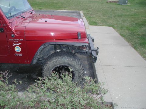 1998 Jeep TJ - A red Jeep Wrangler 4.0L Sport is parked on a concrete path next to a grassy area.