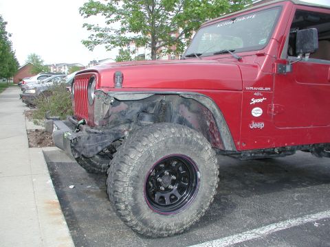 1998 Jeep TJ - A red 1998 Jeep Wrangler 4.0L Sport shows damage to its front bumper and fender, parked on asphalt.