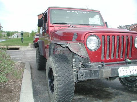 1998 Jeep TJ - Front view of a red Jeep Wrangler, parked outdoors. Another vehicle is seen in the background.