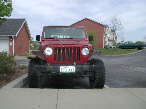 1998 Jeep TJ - A red Jeep Wrangler is parked in a lot, with a green pickup truck visible in the background.